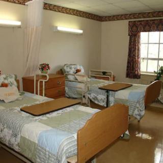 A hospital room with two patient beds, each equipped with bedside tables and a window providing natural light.