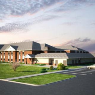 A modern commercial building with a landscaped front and parking area under a partly cloudy sky.