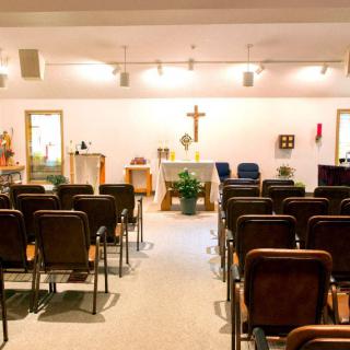 A small chapel interior with rows of seats facing an altar and a cross.