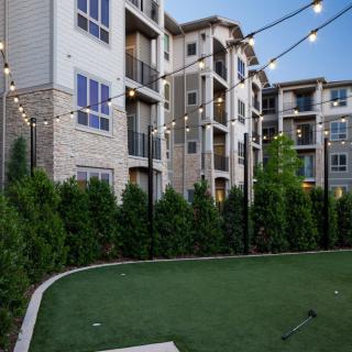 A modern apartment complex with a landscaped outdoor area, illuminated by string lights in the evening.