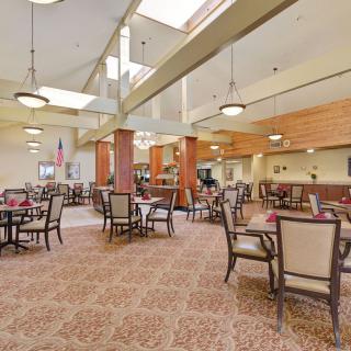 A spacious and elegantly designed dining area with multiple tables and chairs, featuring warm lighting and a carpeted floor.
