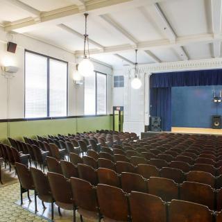 An empty auditorium with rows of seating facing a stage under soft lighting.
