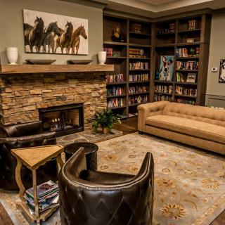 A cozy living room with a fireplace, surrounded by bookshelves and comfortable seating.