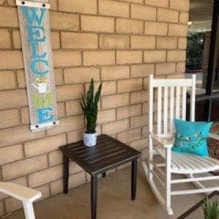 A cozy porch area with a welcome sign, rocking chairs, and a small table with a potted plant.