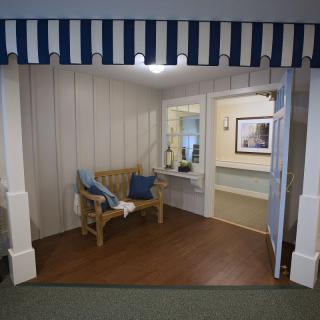 A cozy indoor seating area featuring a wooden bench with blue cushions, under a striped awning.