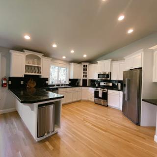 A modern kitchen featuring sleek black granite countertops, white cabinetry, and a warm hardwood floor.