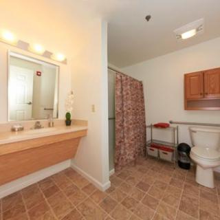 A spacious bathroom featuring a sink with a mirror, a toilet, and a shower area with a curtain. The room has tiled flooring and wall-mounted cabinets.