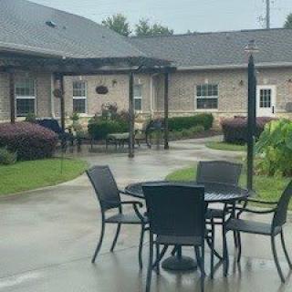 A patio area with tables and chairs, surrounded by a garden and buildings.