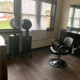 A hair salon with a styling chair and two dryers by the window.