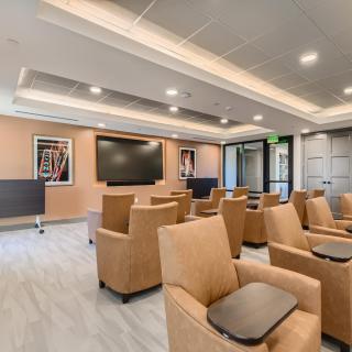 A modern lounge with comfortable seating and a large screen, suitable for meetings or presentations.