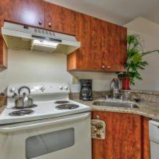A cozy kitchen with wooden cabinets, featuring a stove, oven, coffee maker, and a teapot on the counter.