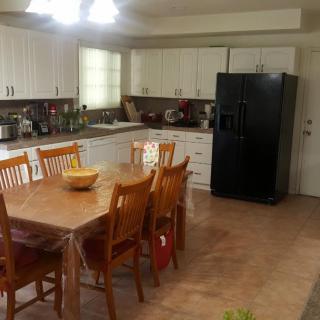 A spacious kitchen with a wooden dining table and chairs, featuring white cabinets and a black refrigerator.