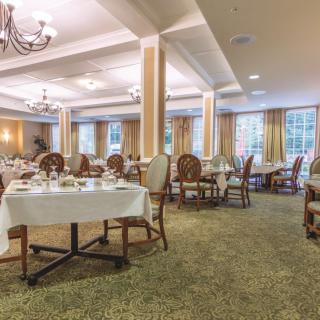 An elegant dining room with neatly arranged tables and chairs, illuminated by chandeliers.