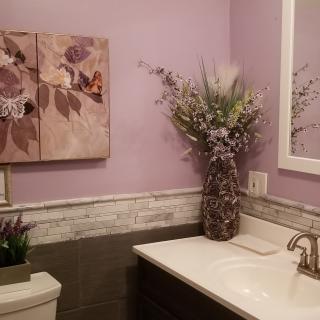 A stylish bathroom with lavender walls, featuring floral artwork and a decorative vase.