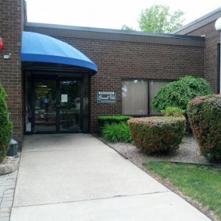 Entrance to a modern building with a blue awning and landscaped surroundings.