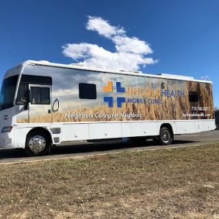 A mobile healthcare clinic parked on a roadside, featuring a design showcasing wheat fields.