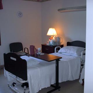 A hospital patient room featuring two beds, a lamp, and a small table.