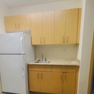 A compact kitchen area with light wood cabinets, a refrigerator, and a small sink.