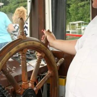 A person steering a boat with a wooden wheel.