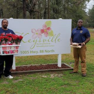 Two men standing in front of a sign displaying the name and address of a flower shop.
