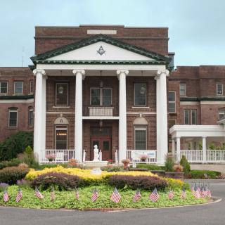 A grand building with large white columns and well-maintained gardens at the entrance.