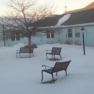 A snowy courtyard with benches and a lamp post during winter.