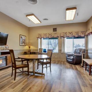 A cozy living room with wooden flooring, featuring a table and chairs set, an armchair, and a television.