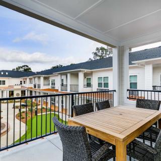A modern apartment balcony with a wooden dining set overlooking the courtyard.
