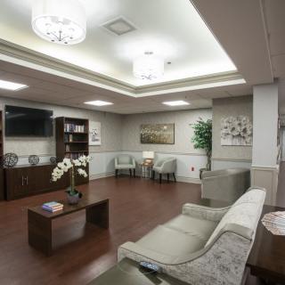 A modern waiting room with comfortable sofas, artwork, and a bookshelf, featuring wooden floors and elegant lighting.