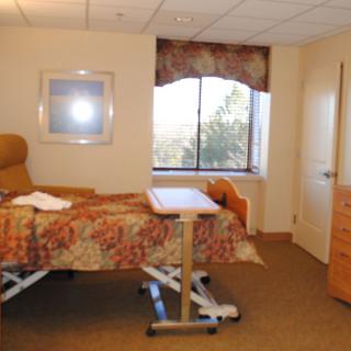 A hospital room with a patient bed and medical equipment, featuring a window and comfortable seating.