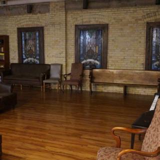A cozy room with wooden flooring, brick walls, and various chairs arranged around the space.