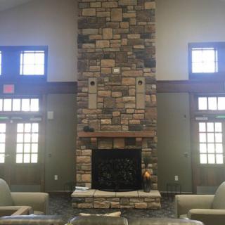 A cozy living room featuring a tall stone fireplace and large windows.