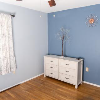 A minimalist bedroom featuring a white dresser against a blue wall with hardwood floors.