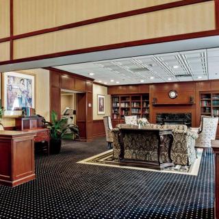 A cozy library interior with bookshelves, a central table surrounded by chairs, and warm wooden decor.