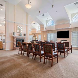 A spacious meeting room with rows of chairs facing a large television and a fireplace.