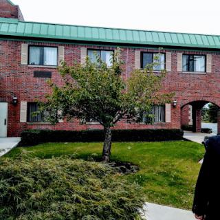 A brick building with a green roof, surrounded by well-maintained landscaping and a tree.