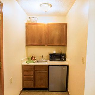 A compact kitchenette featuring wooden cabinets, a mini fridge, and a microwave.