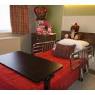 A hospital room with a decorated bed and a table, featuring flowers and gifts.