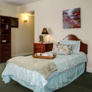 A cozy bedroom with a neatly made bed, decorative pillows, and a nightstand with a lamp and artwork on the wall.