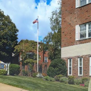 A well-maintained residential building with a flagpole in front, surrounded by lush landscaping.