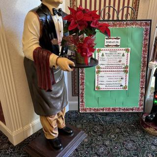 A waiter statue holding a poinsettia next to a holiday-themed menu display.