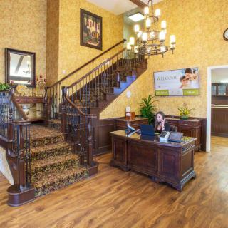 A warmly decorated office lobby featuring a wooden reception desk, ornate staircase, and chandelier.