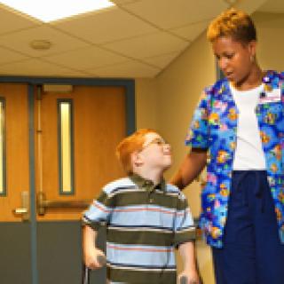 A nurse assists a young child in a hospital hallway.