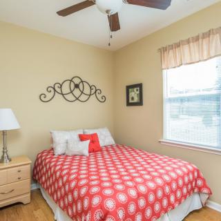 A cozy bedroom with a polka dot bedspread, ceiling fan, and natural light from the window.