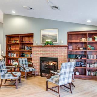A cozy library with a brick fireplace, surrounded by bookshelves and plaid-upholstered chairs.