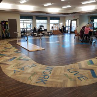A spacious rehabilitation center featuring a welcoming exercise area with various fitness equipment and wooden flooring.