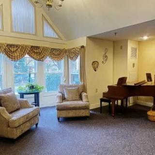 A cozy living room with plush chairs, a grand piano, and large windows adorned with elegant curtains.
