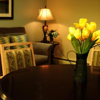 A cozy living room setting featuring a round table adorned with yellow flowers, complemented by a soft lamp and comfortable seating.