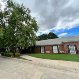 A brick building with a tree and well-maintained lawn under a cloudy sky.