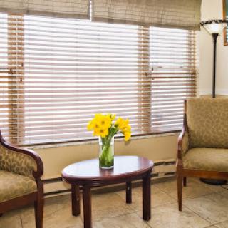 A cozy living room featuring two chairs, a small table with vibrant yellow flowers, and soft natural light filtering through the blinds.